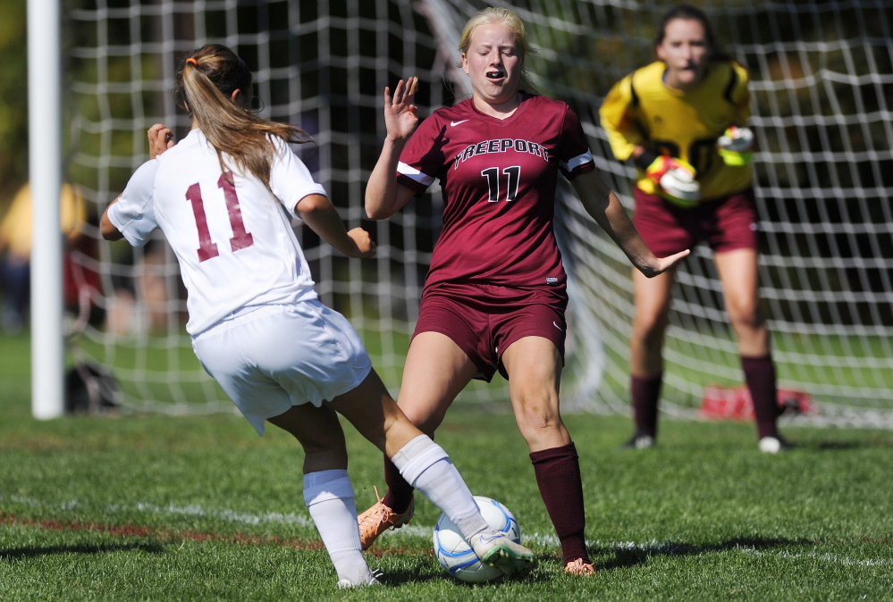 Ellie Schad of Greely looks for a way around defender Lindsay Cartmell of Freeport as goalkeeper Izzy Qualls prepares for a shot during their game in Cumberland Saturday. John Ewing/Staff Photographer