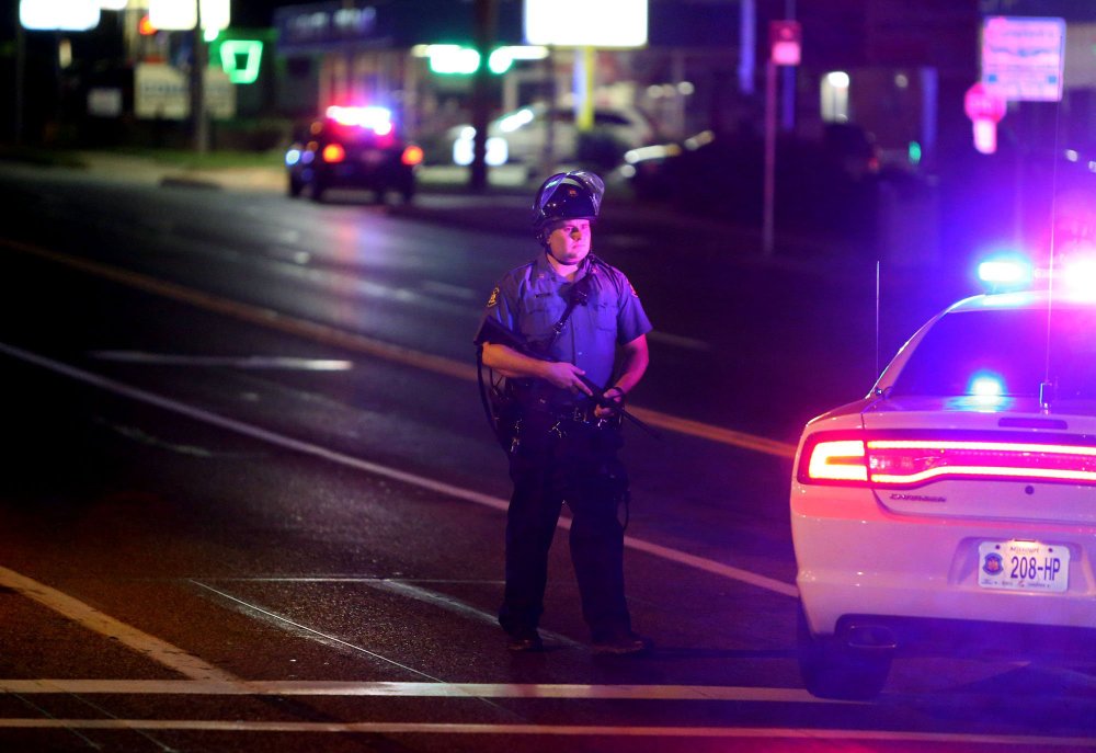 A police  officer stands at Chambers Road at West Florissant on Saturday in Ferguson, Mo.