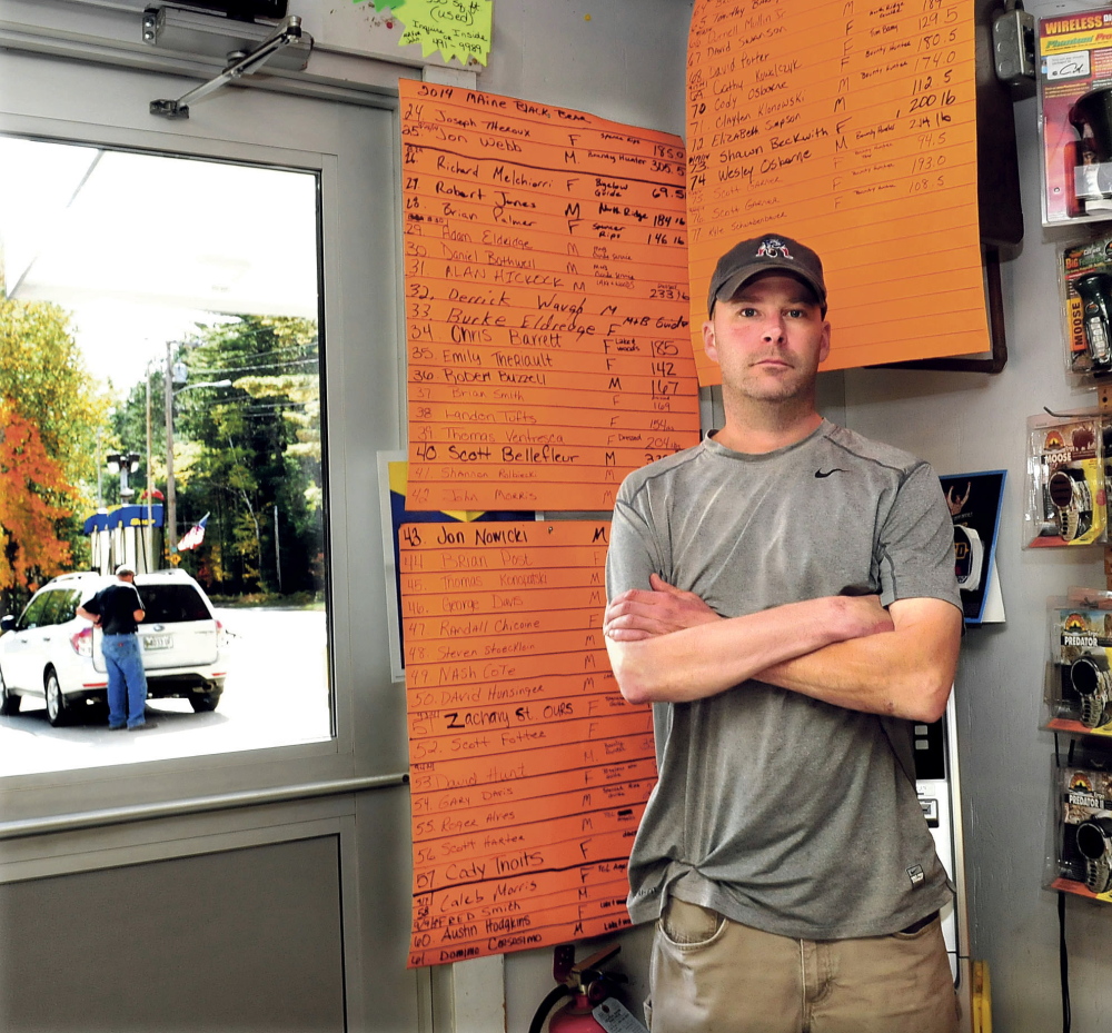 As a customer pumps gasoline outside Pines Market in Eustis, owner John Morris stands beside the tally boards of the 77 bears that have been tagged this season. The number is twice the amount tagged last year. Morris said if the bear referendum passes it would have an adverse impact on his business. “There are plenty of bear around this year,” Morris said.  David Leaming/Morning Sentinel
