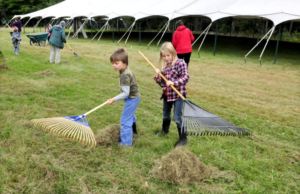 Volunteers Forest Pitkin and Juniper Fowler on Tuesday help rake mowed grass outside a vendor tent while preparing for the three-day Common Ground Country Fair that begins Friday in Unity.