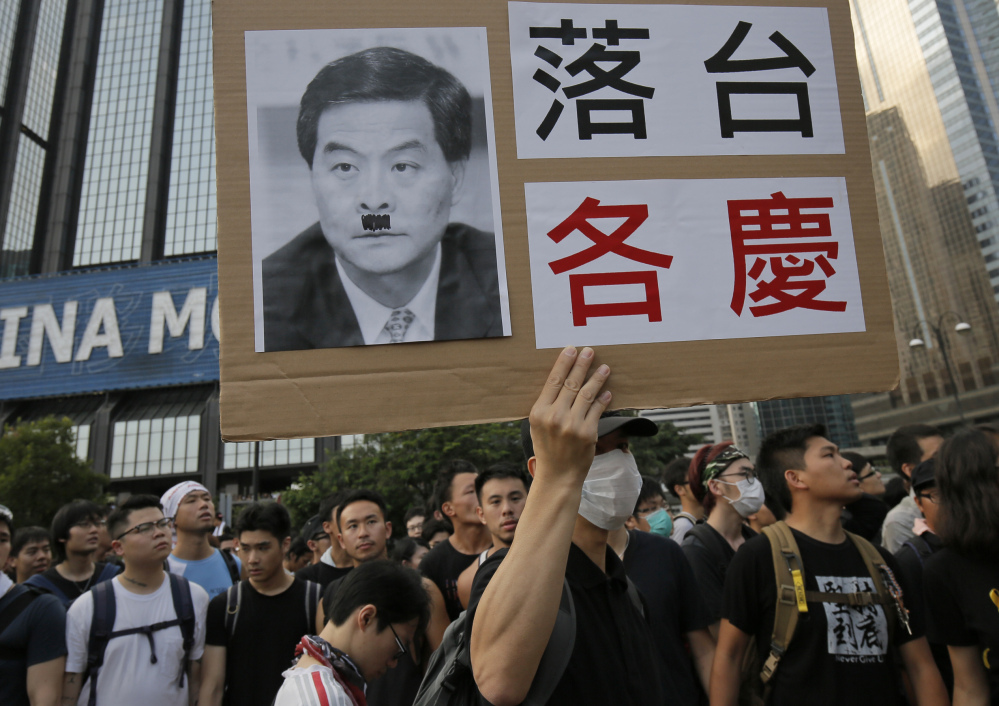 A pro-democracy protester raises a placard with a defaced photo of Hong Kong’s Chief Executive Leung Chun-ying outside a flag-raising ceremony Wednesday.