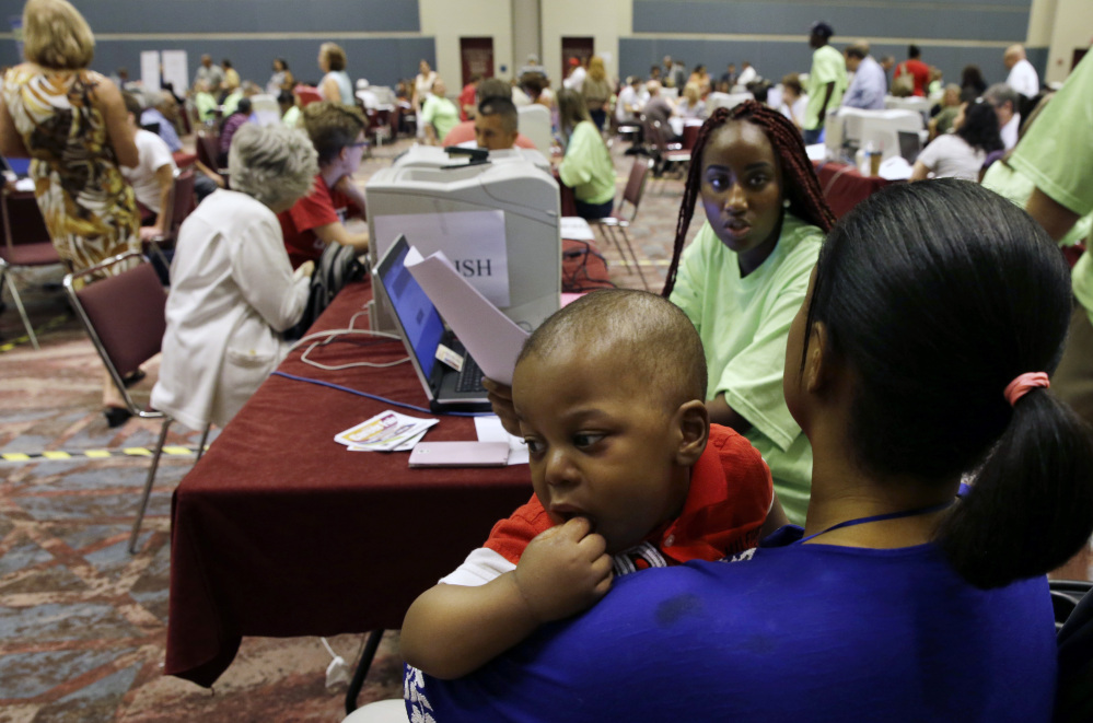 Fatuma Kamara holds her 11-month-old as she gets help from Kristanna Brown in filing for unemployment benefits during a mass session for newly laid-off casino workers last month in Atlantic City, N.J.