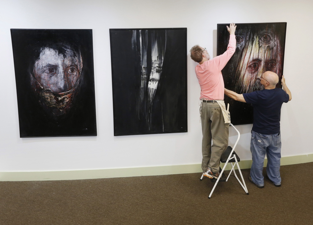 Leonard Meiselman, right, hangs his paintings with help from fellow artist George Mason for “The Dilemma of Memory” at the Holocaust and Human Rights Center of Maine.  Derek Davis/Staff Photographer