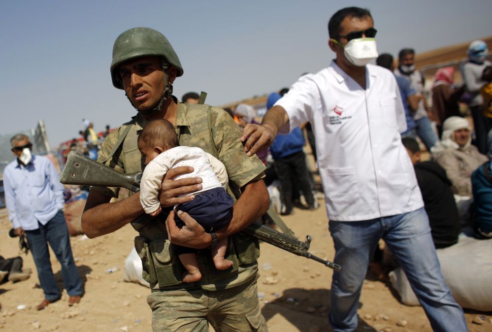 A Turkish soldier carries a Syrian Kurdish refugee baby from the Syrian border town of Kobani, near the southeastern Turkish town of Suruc in Sanliurfa province Thursday. More than 150,000 refugees have fled Kobani over the past two weeks alone, with a steady exodus continuing. Officials from Turkey’s AFAD disaster management agency said some 4,000 crossed Wednesday, and a similar figure the day before. Reuters