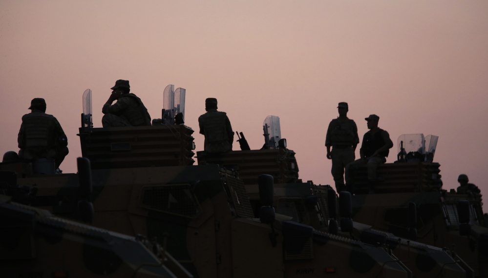 Turkish soldiers are silhouetted as they stand on top of armored vehicles on the Turkish-Syrian border Friday.