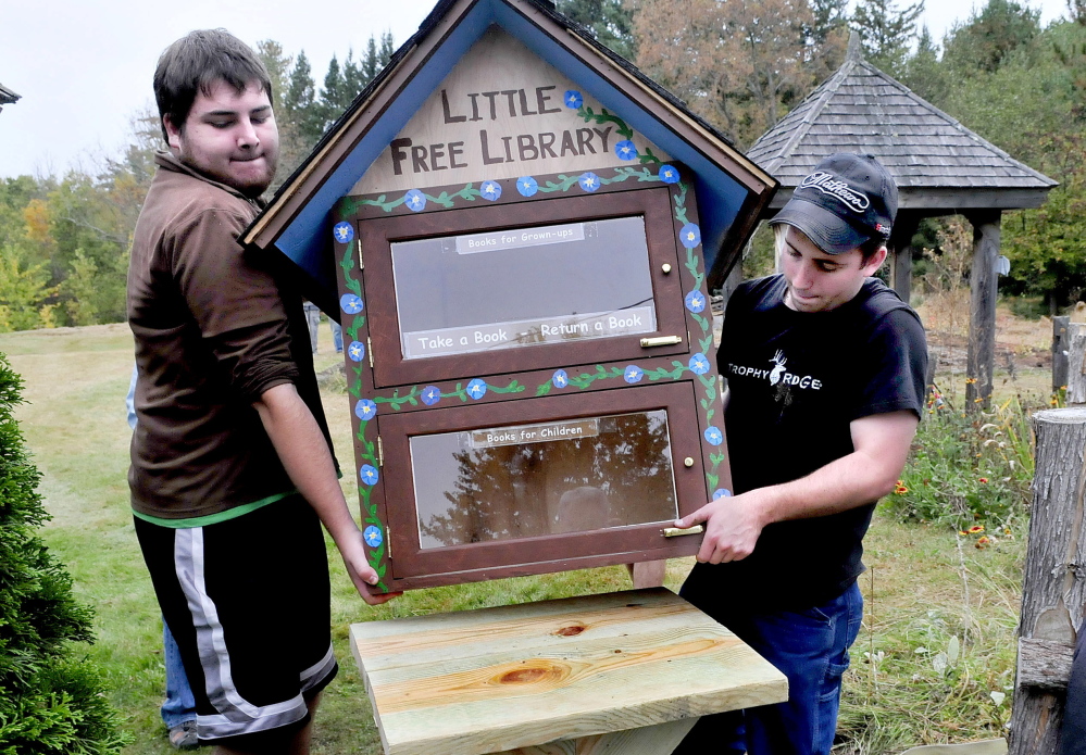 Thomas Ciarlante, left, and Brett Skelly, volunteers from Unity College, place a Little Free Library, where people can donate and borrow books, at Triplet Park in Unity on Saturday.