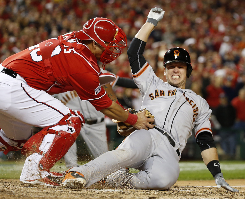 Buster Posey of the San Francisco Giants is tagged out by Washington catcher Wilson Ramos in the ninth inning of San Francisco’s 2-1 victory in 18 innings Saturday night.