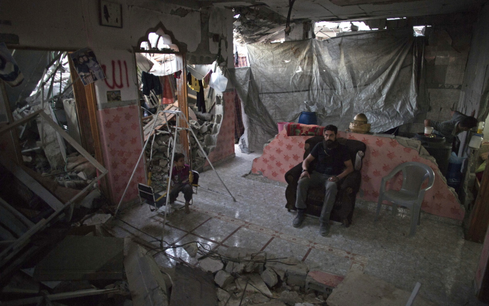 Palestinian Madi Hasanein sits next to his son while he swings in what is left of  their house in Gaza City. Thousands of people whose homes were destroyed or damaged in the Israel-Hamas war still live in classrooms, storefronts and shelters.