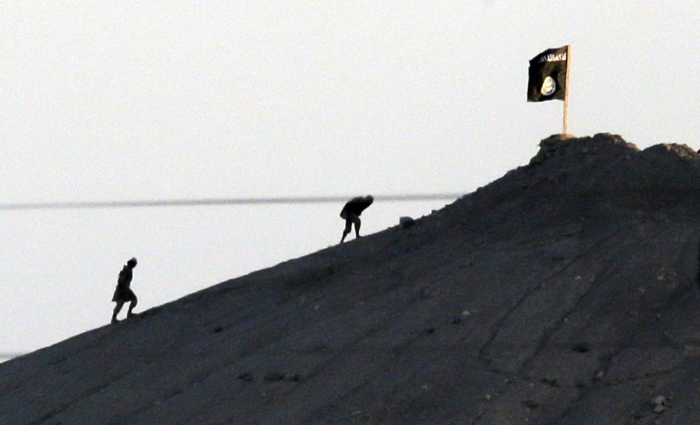 Islamic State militants are seen after placing their group’s flag on a hilltop at the eastern side of the town of Kobani, Syria, where fighting with Syrian Kurds intensified Monday.