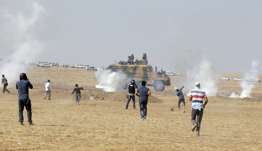 Turkish Kurds in the outskirts of Suruc, at the Turkey-Syria border, run to throw stones towards a Turkish forces armoured vehicle firing tear gas to disperse them after they gathered as fighting intensified between Syrian Kurds and the militants of Islamic State group, in nearby Kobani, Syria, Tuesday.