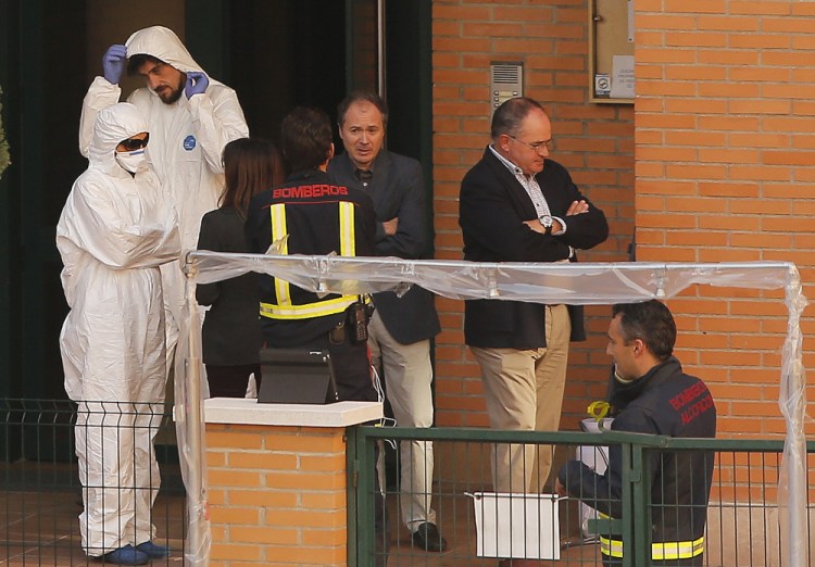 Firemen stand as worker wearing rompers and gloves come out ofthe building entrance of the apartment building of the Spanish nurse infected with Ebola in Madrid, Spain, Wednesday.