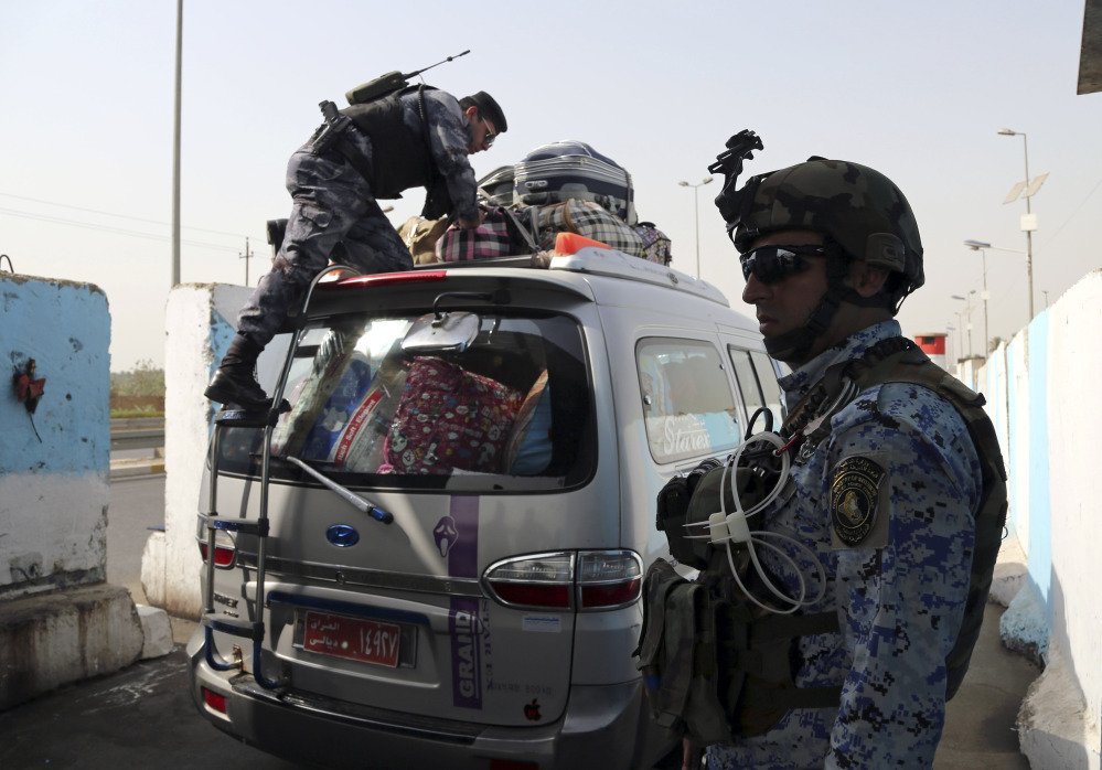 An Iraqi federal policeman stands guard as his colleague searches a car at a checkpoint in Baghdad, Iraq, on Saturday.