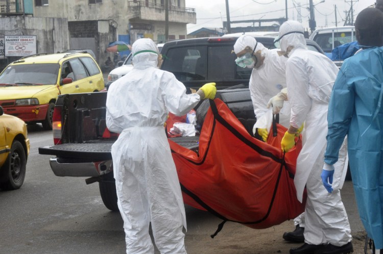 Health workers in protective gear carry the body of a person suspected to have died from Ebola on the street of  Monrovia, Liberia.