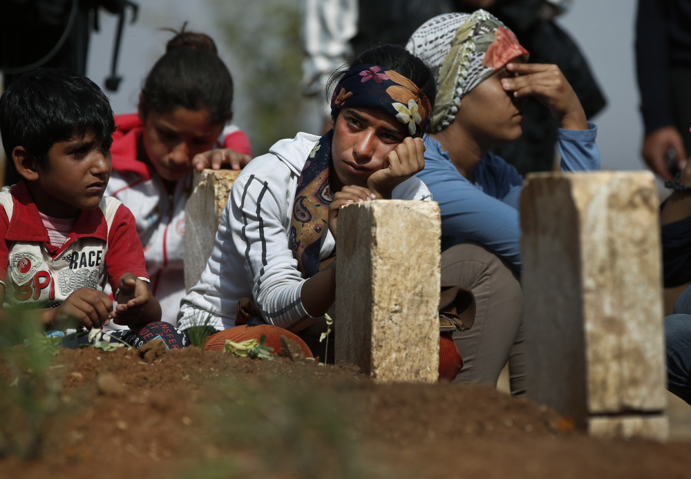 Kurdish people sit by the grave as they mourn their loved one, a Kurdish fighter, name not given, who was killed in the fighting with the militants of the Islamic State group in Kobani, Syria, and was buried at a cemetery in Suruc, on the Turkey-Syria border.
