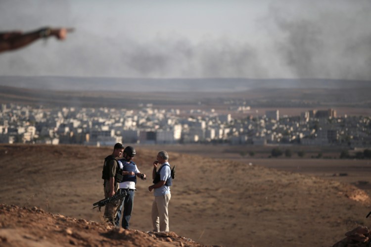 Members of the media talk with a Turkish soldier, left, on a hilltop on the outskirts of Suaruc, at the Turkey-Syria border, overlooking Kobani, Syria, background, during fighting between Syrian Kurds and the militants of Islamic State group, Wedesday.