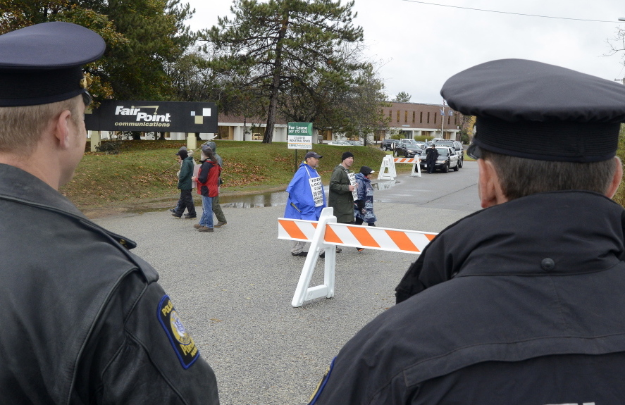 Police Sgt. Jason King and Officer Christian Stickney keep an eye on a handful of pickets Wednesday on a wet and windy day outside FairPoint headquarters in Portland.