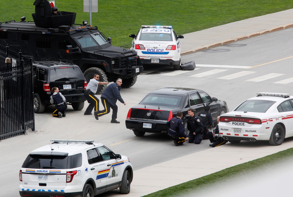 In a country that rarely sees gun violence, police officers take cover near Parliament Hill after a Canadian soldier was fatally shot Wednesday at the Canadian War Memorial in Ottawa.