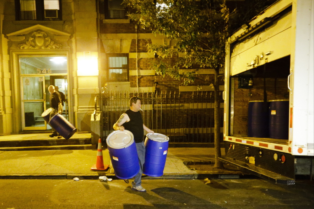 Workers from BioRecoveryCorp carry barrels from the apartment building of Ebola patient Dr. Craig Spencer Friday, Oct. 24, in New York. Spencer remained in stable condition while isolated in a hospital, talking by cellphone to his family and assisting disease detectives who are accounting for his every movement since arriving in New York from Guinea via Europe on Oct. 17.