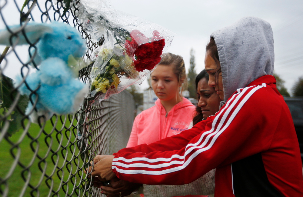 Student Tyanna Davis, right, places flowers on the fence bordering Marysville Pilchuck High School in Marysville, Wash., on Saturday, a day after a student opened fire, killing one person and wounding others before dying of a self-inflicted gunshot.