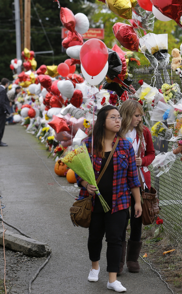 Francesca Tuazon, left, and Nicole Buell bring flowers and balloons to a growing memorial on a fence around Marysville-Pilchuck High School on Monday.