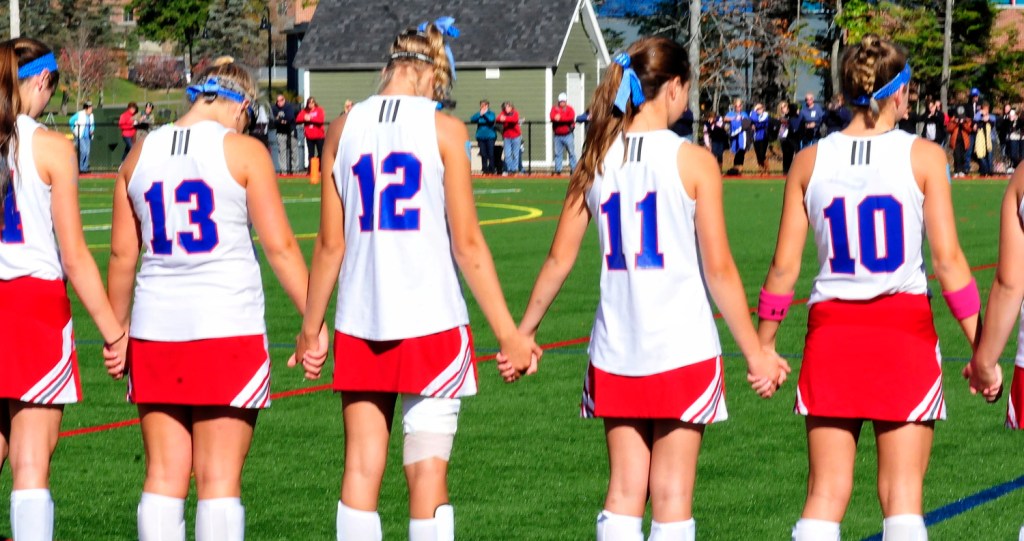 In a sign of respect and support, members of the Messalonskee field hockey team hold hands Monday during a moment of silence for student and soccer player Cassidy Charette who died in a hayride accident over the weekend. Players and fans also wore blue ribbons in her memory.