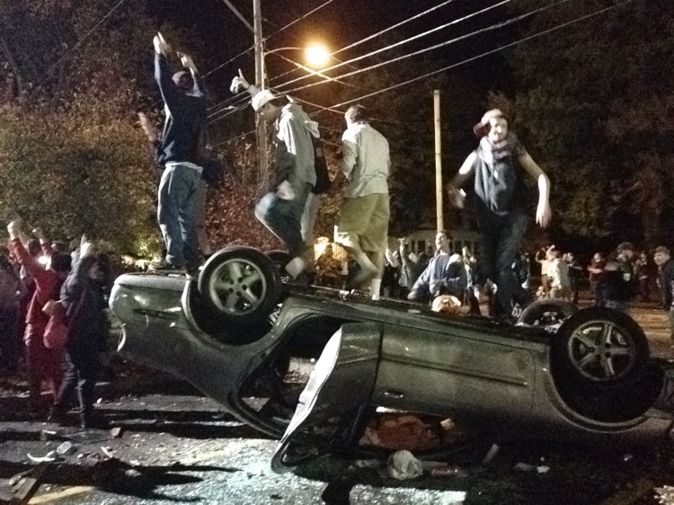 People stand atop an overturned car in Keene, N.H. on Saturday during a night of violent parties that led to destruction, dozens of arrests and multiple injuries, near the city's annual pumpkin festival.  The Associated Press/The Boston Globe, Jeremy Fox