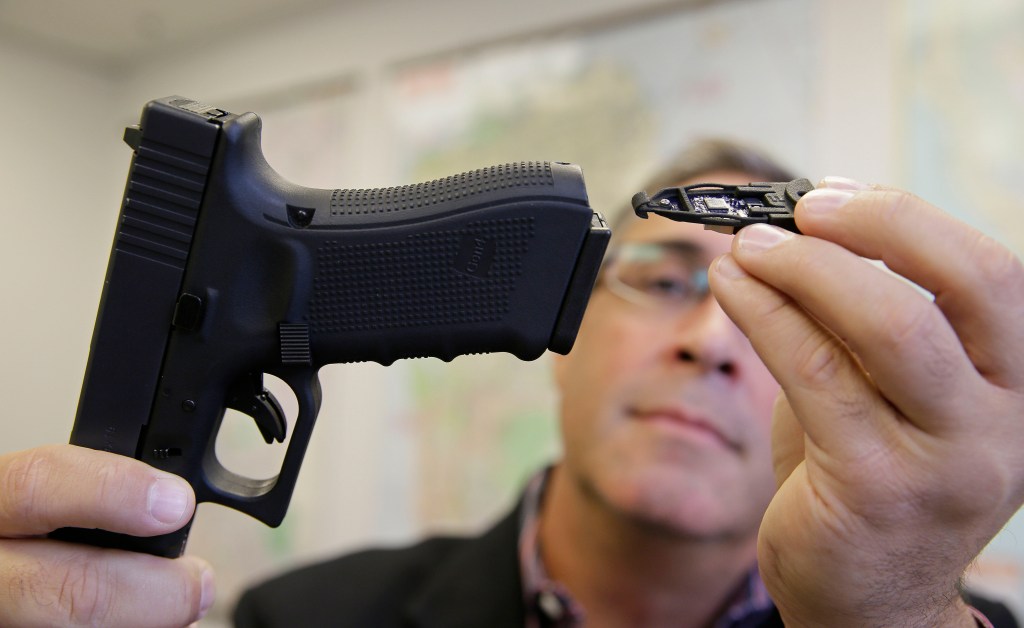 Jim Schaff, vice president of marketing with Yardarm, demonstrates how a sensor fits into an Airsoft replica of a Glock 17 handgun. The Associated Press. 