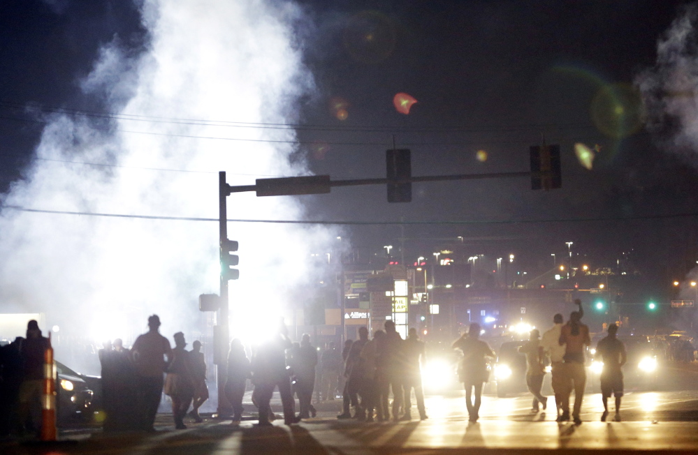 In this Aug. 18 file photo, people stand near a cloud of tear gas in Ferguson, Mo., during protests for the Aug. 9 shooting of unarmed black 18-year-old Michael Brown by a white police officer. The U.S. government agreed to a police request to shut down several miles of airspace surrounding Ferguson, even though authorities said their purpose was to keep media helicopters away during protests in August, according to recordings of air traffic control conversations obtained by The Associated Press.