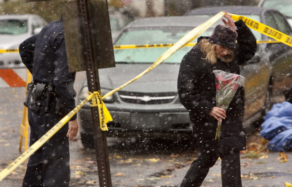 A police officer assists a woman preparing to add flowers to a growing memorial for the fire victims. The woman would not give her name, but said she knew a girl who died in the fire.