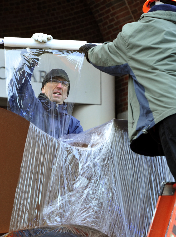 Kris Kenow and Greg Welch shrink-wrap the sculpture before it is lifted by a crane.