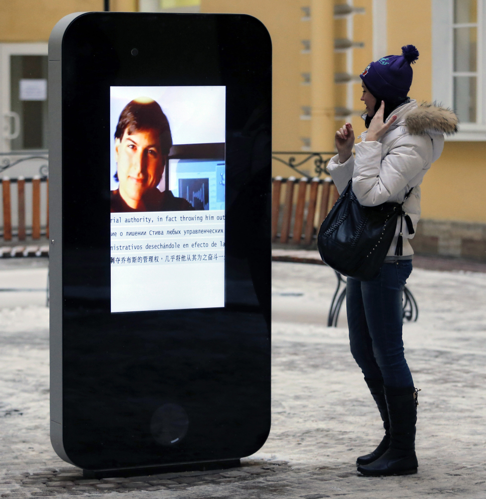 A woman looks at a screen showing a portrait of Steve Jobs on the memorial to the late Apple Corp. co-founder in 2013.