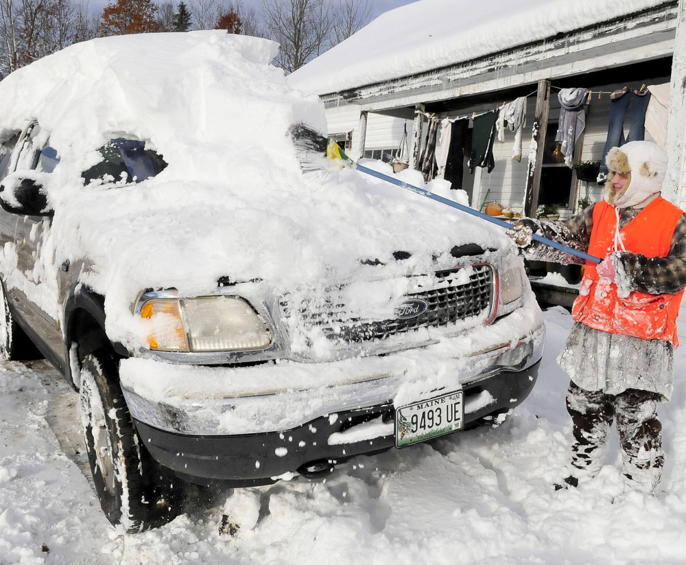 NOV. 3: Sydney Astbury uses a broom Monday to clear the nearly foot of snow that buried the family vehicle at her home in Troy. Many towns near Troy were without power as wind and heavy snow hit the area Sunday.
