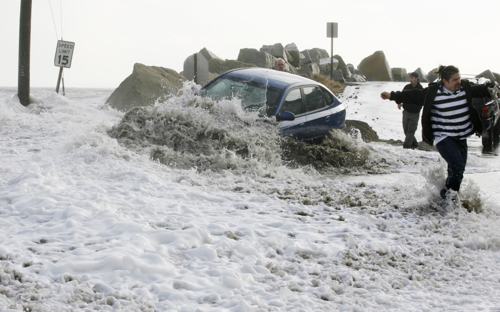 A wave breaks over an occupied car as people try to tow it to safety on Feb. 26, 2010, at Camp Ellis in Saco. The driver left the car as the tide continued to rise, flooding local streets.