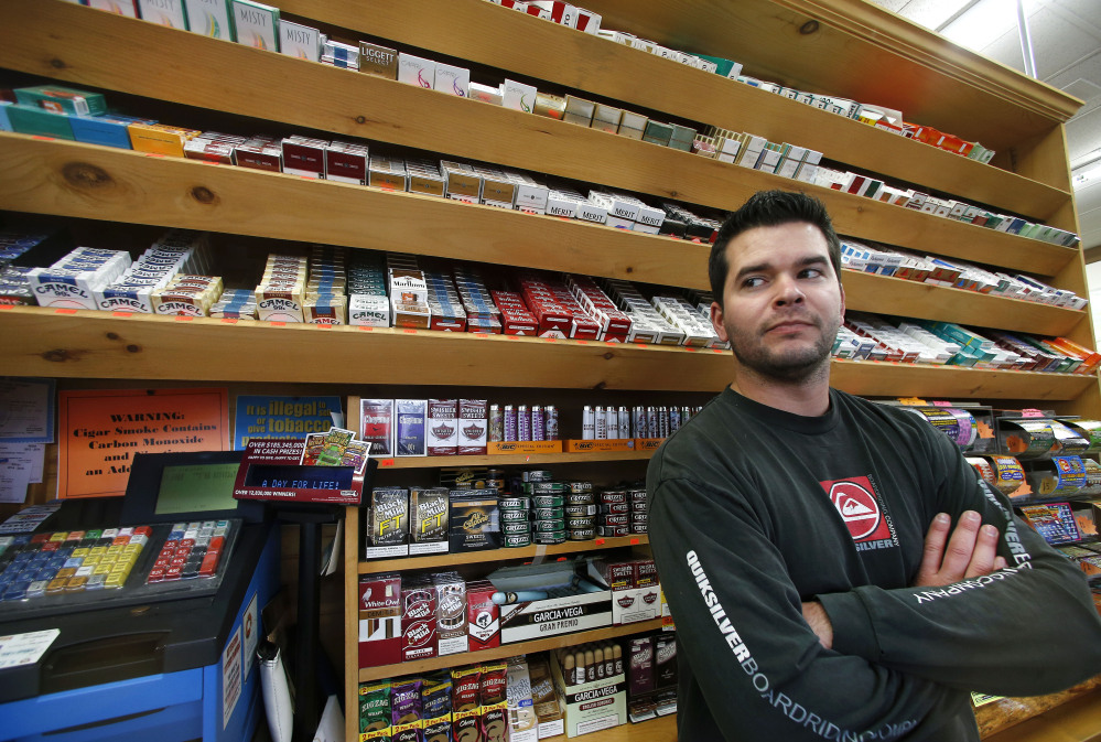 Brian Vincent poses in front of a large display of tobacco products at Vincent’s Country Store in Westminster, Mass. Local officials are contemplating what could be a first: a blanket ban on all forms of tobacco and e-cigarettes, leaving some shop owners fuming.