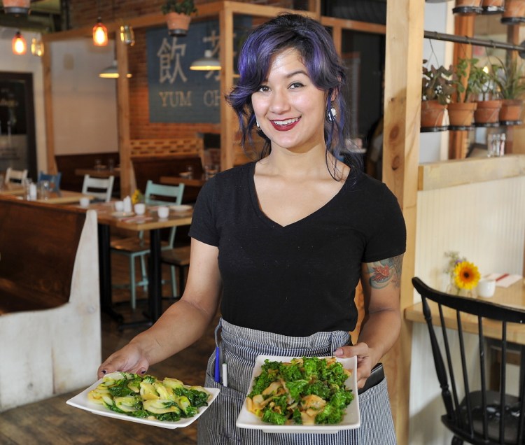 Empire Chinese Kitchen waitress Trish Riggs with two of the restaurant’s dishes that emphasize leafy greens.