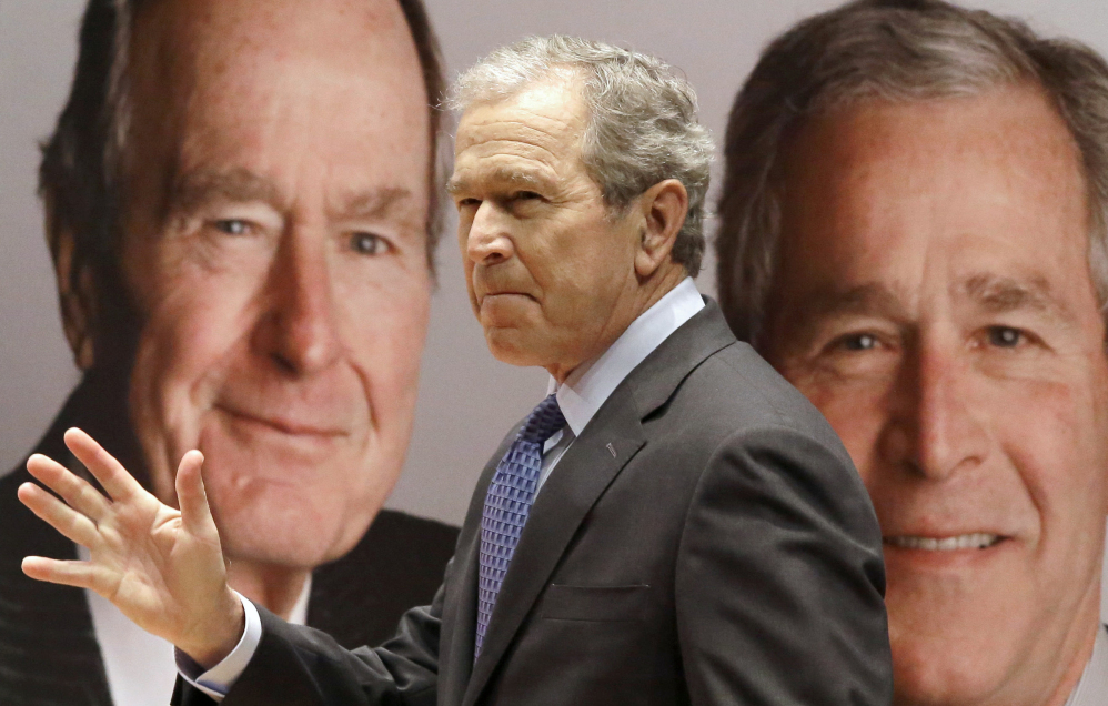 Former President George W. Bush passes by a portrait of himself and his father, former President George H.W. Bush, as he takes the stage to discuss his new book, “41: A Portrait of My Father” at the his father’s presidential library Tuesday in College Station, Texas.