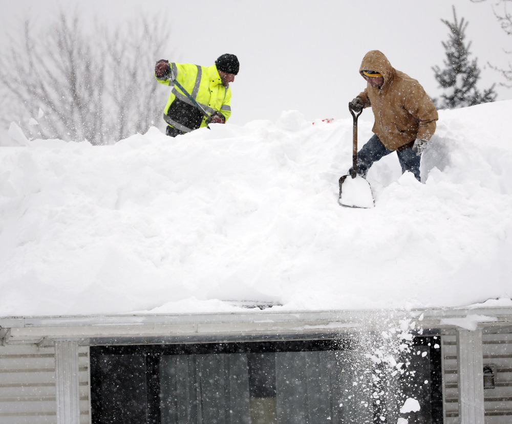 Mark Settlemyer, left, gets help from Ken Wesley clearing snow from the roof of his mother’s house in Lancaster, N.Y., as residents worry about roofs buckling from the weight.