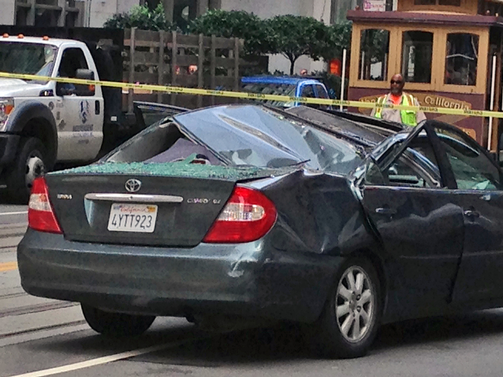 Police and citizens look over a car that has a caved-in roof after a window washer fell at least 11 stories onto the vehicle while it was making a turn in San Francisco on Friday.