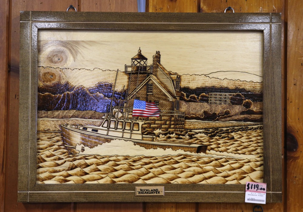 A wood-burned etching depicting the nearby Rockland Breakwater lighthouse is displayed for sale at the Maine Prison Store on Friday in Thomaston. The Maine prison system has two stores that sell the handicrafts of inmates – everything from bookshelves to a model of the USS Constitution.
