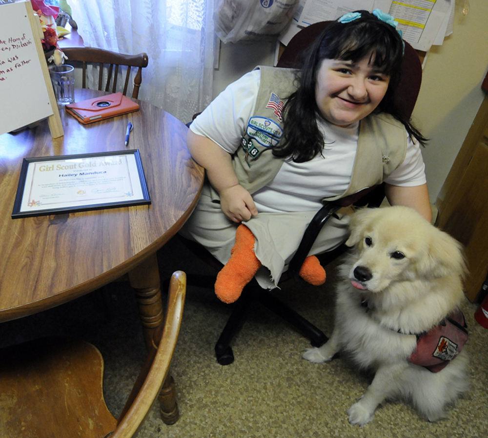 Hailey Manduca, 16, sits with her service dog at home in Bourne, Mass. Born with brittle bone disease, she excels in Girl Scouts and has earned its top honor: the Gold Award.