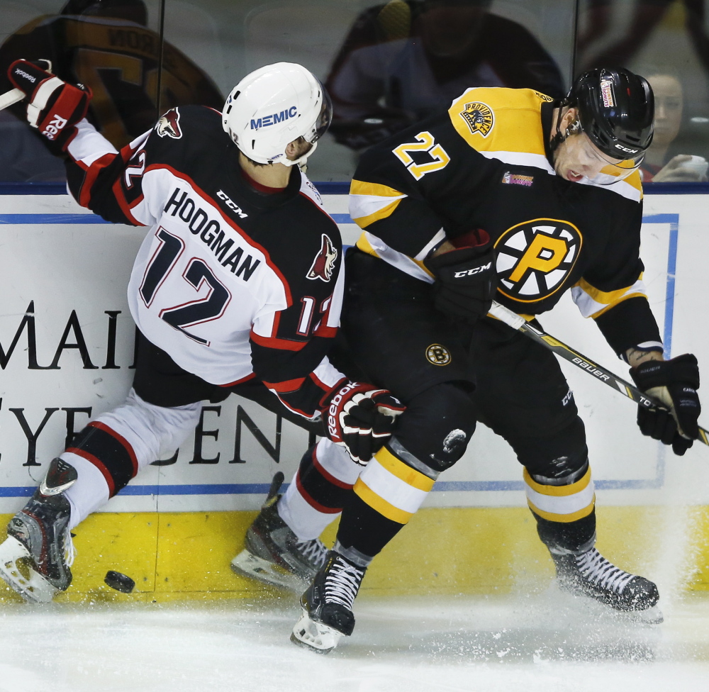 Justin Hodgman of the Portland Pirates, left, starts a spill to the ice while competing for the puck along the boards with Jordan Caron of the Providence Bruins.