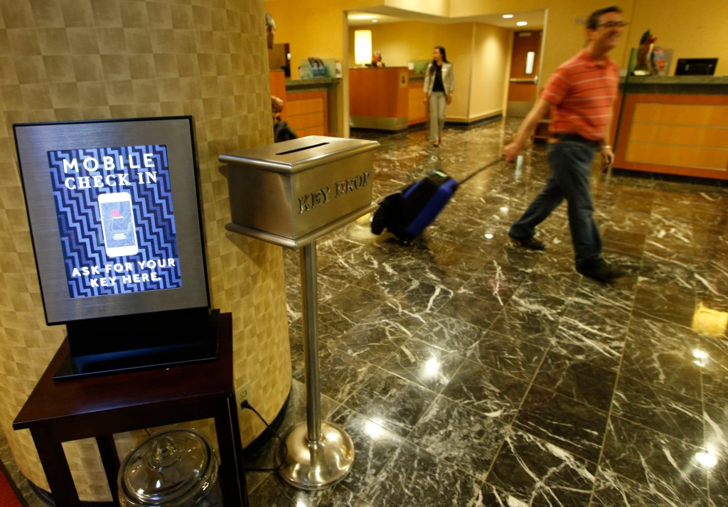 In this Oct. 14, 2014, photo, hotel guest J.D. Solomon, of Indianapolis, right, strolls out of the lobby after using the mobile check-in counter at the Marriott Marquis Times Square hotel in New York. Marriott International launched the ability to check in through its app at 330 North American hotels last year. By the end of this year, the program will be live at all 4,000 hotels worldwide. The Associated Press