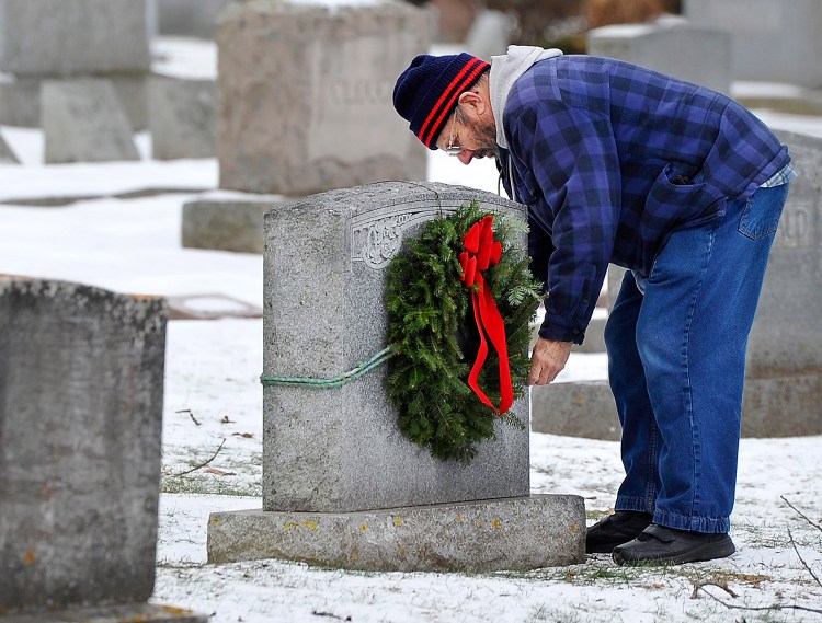 In this Dec. 8, 2014, Charlie Davis of Old Orchard Beach replaces the wreath that was stolen from the headstone of the grave of his parents and grandparents in Laurel Hill Cemetery in Saco.