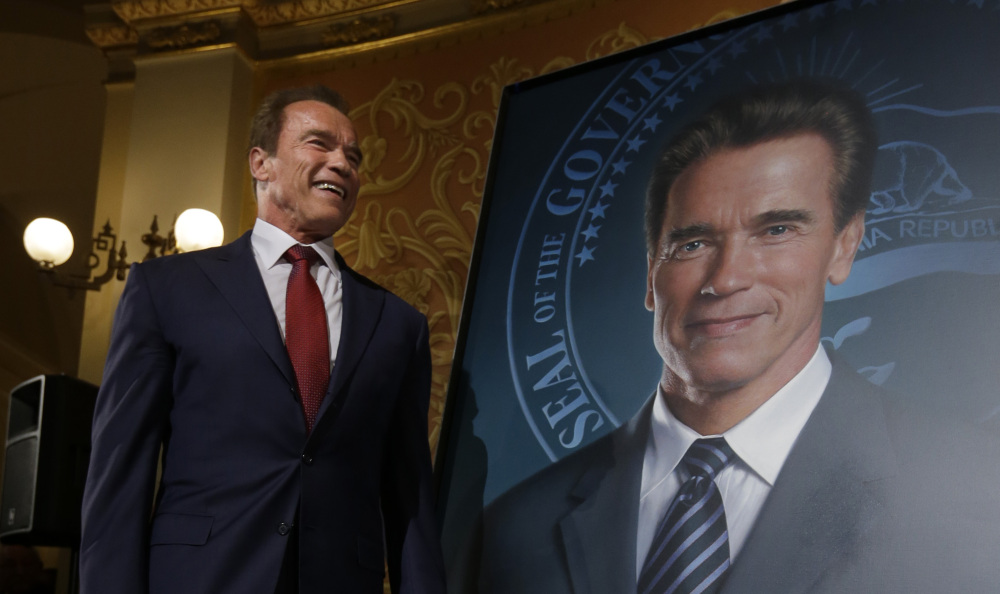 Arnold Schwarzenegger stands next to his official portrait, which used to feature a smudge that has now been fixed.