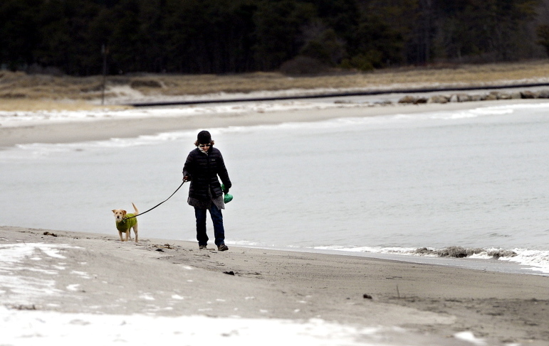 Francine O’Donnell of Portland takes a frigid walk along Pine Point Beach in Scarborough with her dog Grace on Monday afternoon. Warmer weather is expected to bring moisture with it today, with rain predicted along the coast and a foot or more of snow expected in the mountains.
