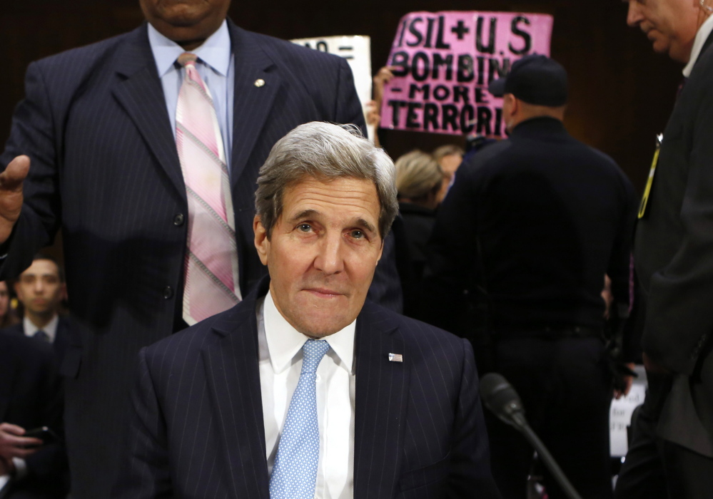 Protesters hold signs as Secretary of State John Kerry testifies before a Senate Foreign Relations Committee hearing Tuesday. Kerry asked for expanded war powers as the United States battles Islamic militants in Syria and Iraq.