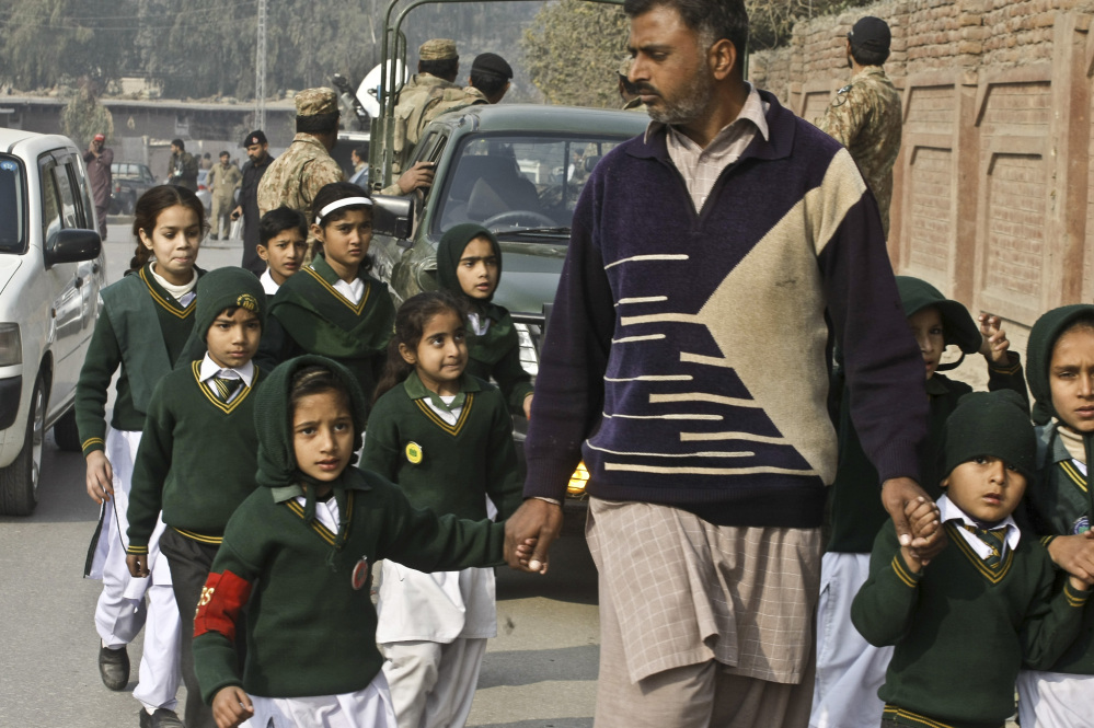 A plainclothes security officer escorts students evacuated from a school as Taliban fighters attack another school nearby in Peshawar, Pakistan, Tuesday.