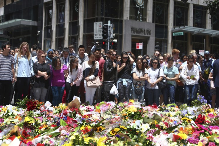 Staff members from the Lindt Chocolat Cafe with their arms linked pay tribute to their colleague who lost his live during a siege at the popular coffee shop at Martin Place in the central business district of Sydney, Australia, Tuesday.
