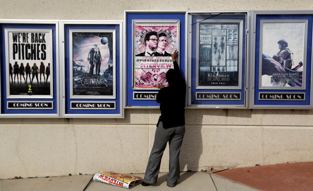 A poster for the “The Interview” is taken down by a worker Wednesday at a Carmike Cinemas theater in Atlanta. Georgia-based Carmike Cinemas and other chains canceled showings of the film in response to threats, before Sony Pictures Entertainment canceled the film’s Christmas release.