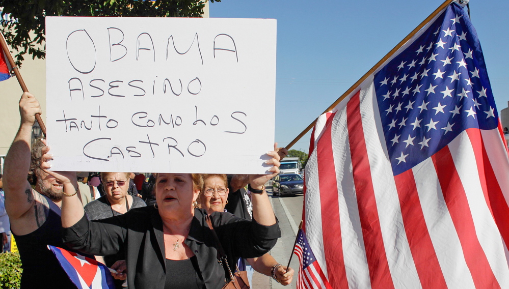 A woman carries a sign reading “Obama is a murderer just like Castro,” at a protest in Miami’s Little Havana on Wednesday. The president’s move toward normalizing ties with Cuba immediately came under attack.